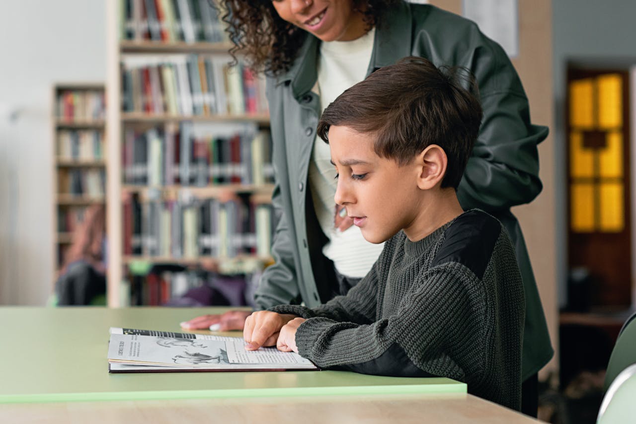 A young boy engages with a book in a library under guidance, fostering a love for learning.